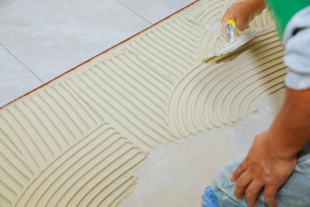 Spreading wet mortar before applying tiles on bathroom floor. puts adhesive